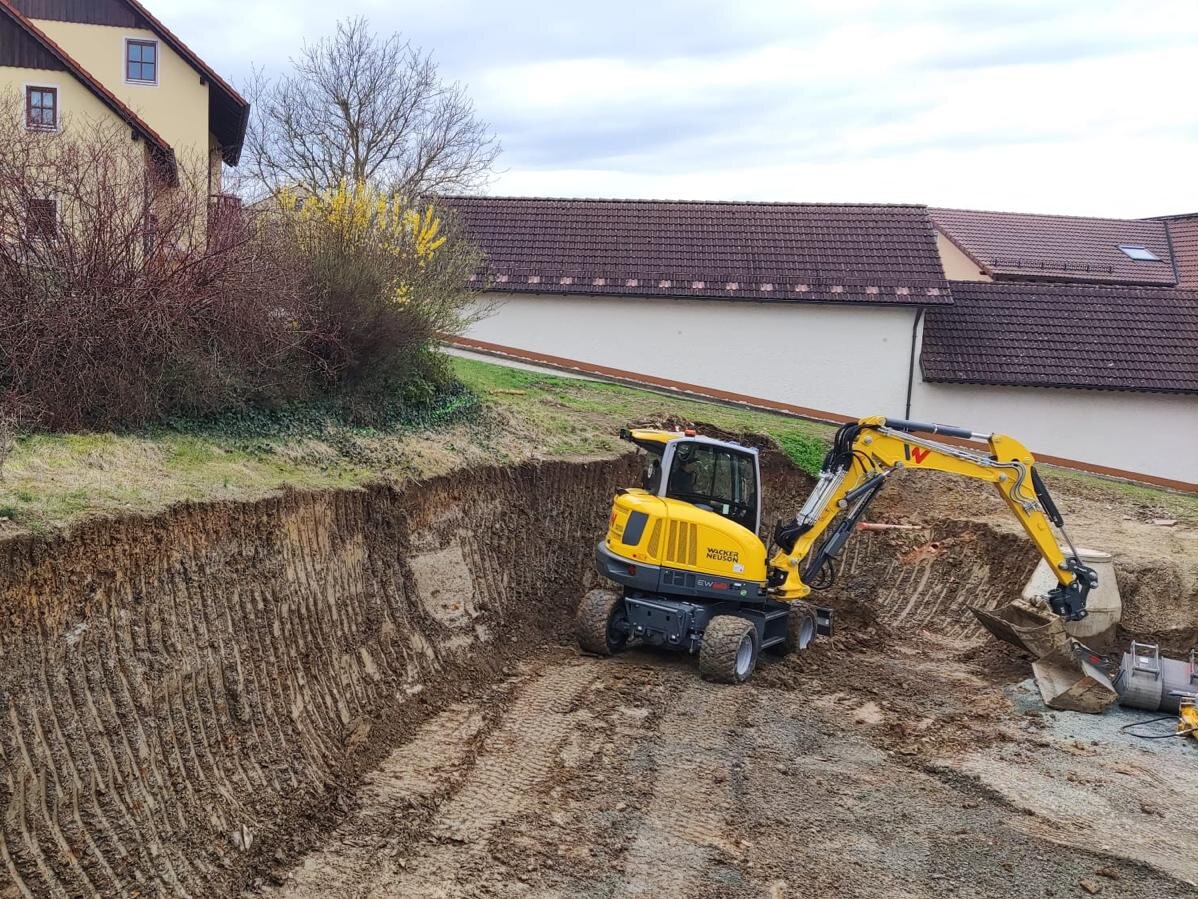 Mobilbagger beim Erdaushub und Gelaendemodellierung an einer Baugrube