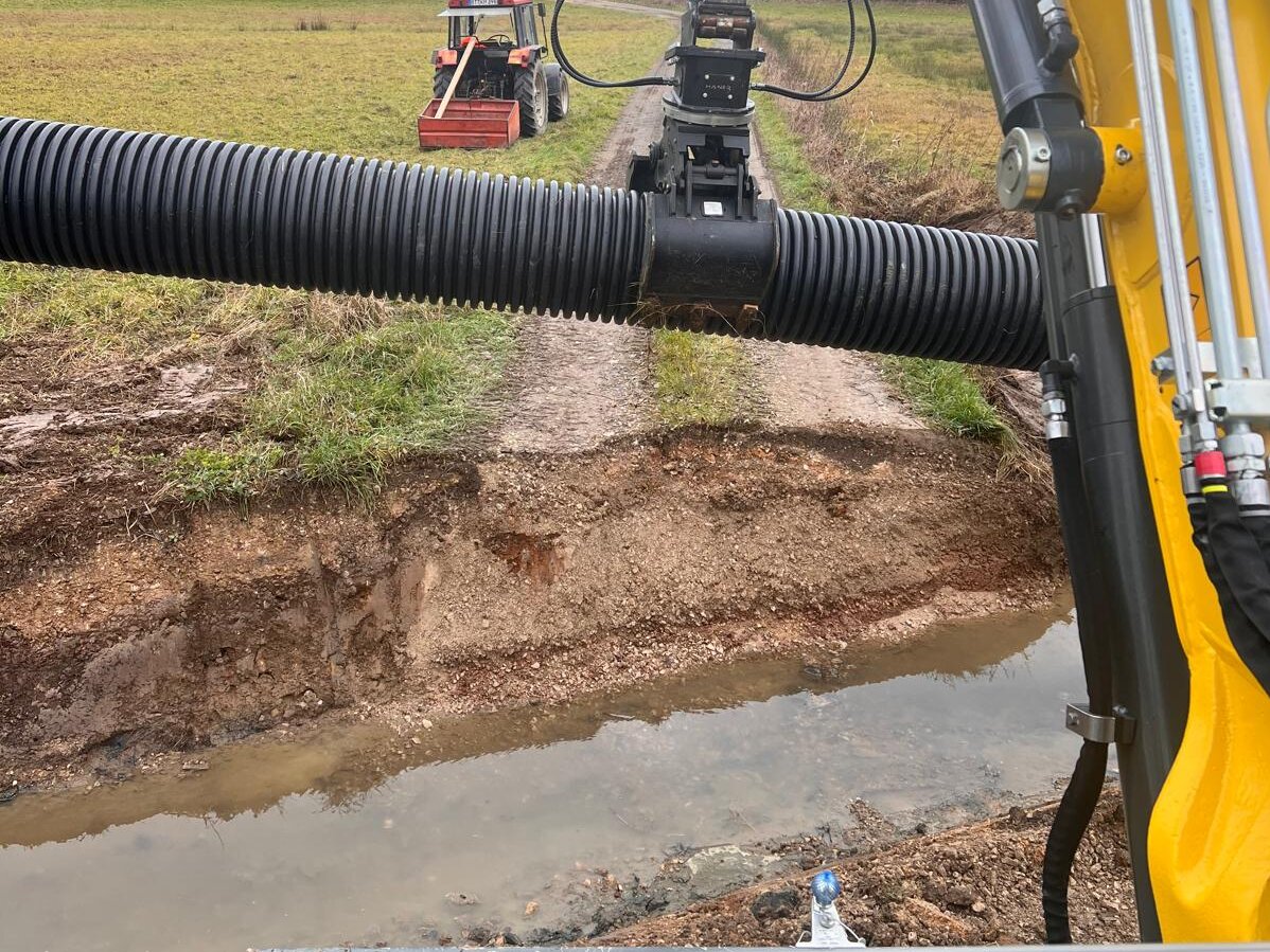 Bagger beim Verlegen eines Drainagerohrs ueber einen Graben